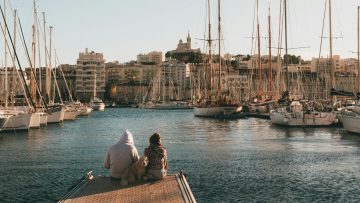 Couple and dog relaxing by the harbor with Marseille skyline.